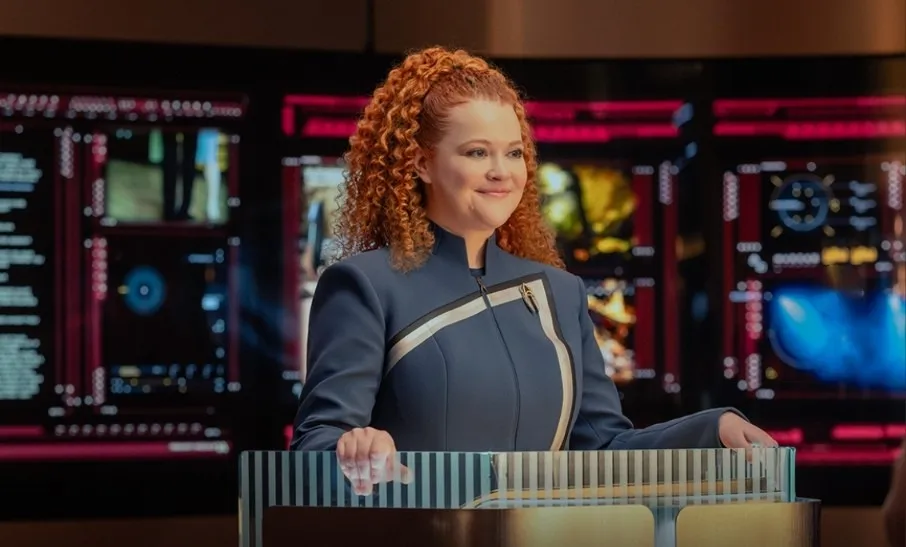 Professor Tilly standing at a lectern before a wall of screens, smiling.