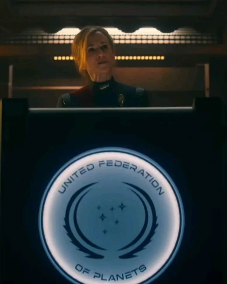 Captain Ake behind a podium bearing the seal of the United Federation of Planets, during sentencing.
