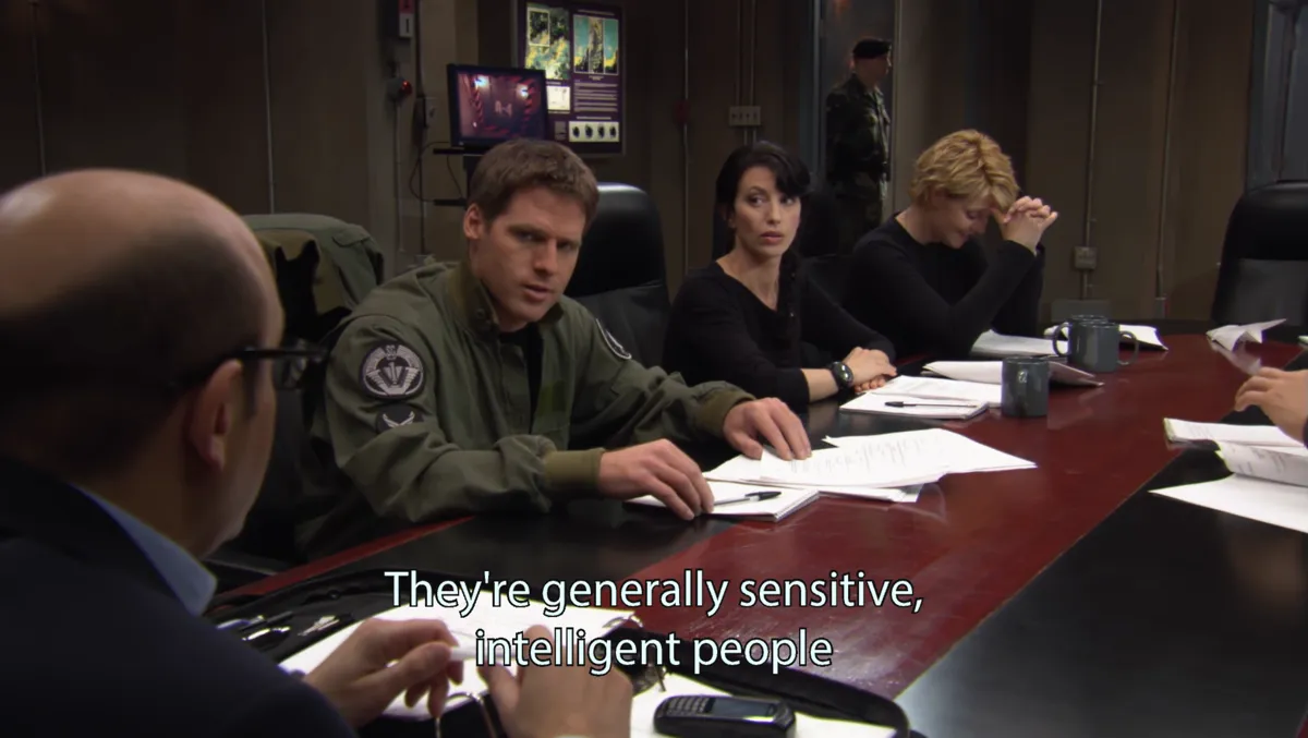 Mitchell, Vala and Carter listen at the briefing table. Subtitle: "They're generally sensitive, intelligent people"